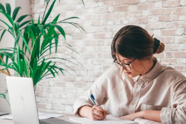 Gülümseyen kadın notlar yazıyor. Dizüstü bilgisayarda webinar çalışmalarını izliyorlar. Genç öğrenci bilgisayar dersi öğreniyor.