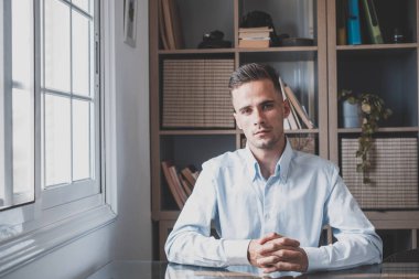 Evde genç bir erkeğin portresi. Çekici beyaz adam bağımsız çalışıyor kameraya bakıyor ve poz veriyor.. 