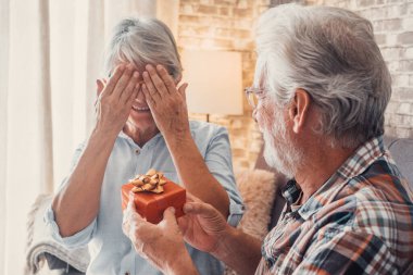 Evde birlikte eğlenen iki tatlı ve yaşlı yaşlının portresi. Olgun bir adam karısına yılbaşı ya da yıldönümü hediyesi veriyor. Şaşkın emekli kadın şimdiki zamana bakıyor.. 