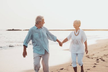 Bir çift olgun insan kumsalda birlikte yürüyor ve kumsalın kumlarında eğleniyor ve anın tadını çıkarıyor. Aşık iki son sınıf öğrencisi eğleniyor. Suyun üzerinde yalınayak yürüyorum