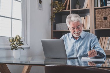 İnternette çalışırken gülümseyen Kafkasyalı mutlu iş adamı laptopta webinar podcast izliyor ve eğitim konferansını öğreniyor notlar alıyor çalışma masasına oturuyor, e-öğrenim kavramı oluşturuyor.