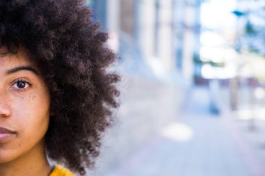 Genç ve güzel bir Afrikalı ya da Amerikalı kadının yarım portresi kameraya bakıyor. Afro kızın gözlerini kapat, kopyala ve boşluğu boşalt 