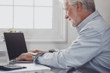 Kafkas iş adamı ya da muhasebecinin dizüstü bilgisayarda yazı yazıp online iş yaptığı bir profil. Kendinden emin gülümseyen kıdemli adam, ev ofisinde çalışan klavyede daktilo kullanıyor.