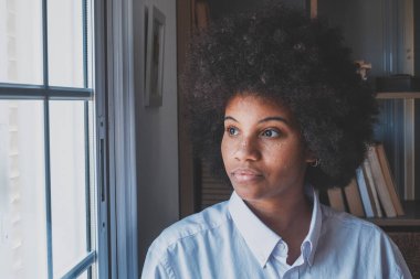 Ofis penceresinden dışarı bakan ciddi Afro-Amerikan iş kadını. Derin düşüncelere dalmış kıvırcık saçlı bir kadın yönetici sorununa bir çözüm düşünüyor. İş yerinde düşünceli bir bayan. 