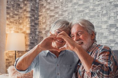 Parmaklarıyla kalp şekli oluşturan iki yetişkin büyükanne ve büyükbabanın ellerine yakın durun. Gülümseyen ve aşkta eğlenen insanlar.. 