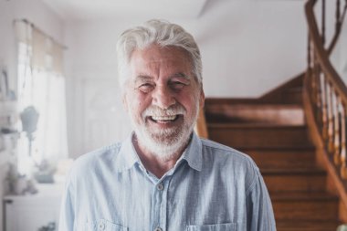 Gri saçlı mutlu yaşlı adam, 80 'li yaşlarda evde beyaz dişleriyle gülümsüyor. İçerde rahatlayan neşeli bir büyükbabanın portresi.. 