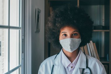 Kendini koronavirüs salgınından korumak için tıbbi maske takan kadın sağlık görevlisi. Profesyonel Afro-Amerikan kadın doktor portresi koruyucu bir maske takıyor ve kameraya bakıyor.