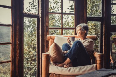 Son sınıf öğrencisi kadın kanepeye oturmuş, elinde kahve fincanı tutarak eve bakıyor. Oturma odasındaki kanepede dinlenen yaşlı kadın. Evdeki kanepede kahve içen düşünceli kadın.  