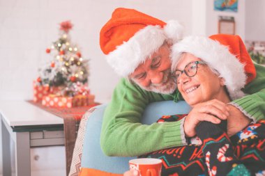 Kalın elbiseli son sınıf çifti ve Noel Baba şapkası evde süslenmiş Noel ağacının önünde el ele tutuşuyorlar. Yaşlı ve romantik heteroseksüel çift Noel festivalini birlikte kutluyor.
