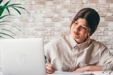 Gülümseyen kadın notlar yazıyor. Dizüstü bilgisayarda webinar çalışmalarını izliyorlar. Genç öğrenci bilgisayar dersi öğreniyor.
