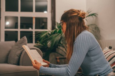 Bir tanesi sevimli ve çekici, gözlük takıyor, kitap okuyor ve evde kanepede ilginç bir kitap izliyor. Genç bir kadın geceleri yalnız başına kanepede oturmuş kitap okuyor.. 