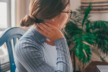 One young woman feeling bad and having pain for over studying at home on the table. Backache concept. Portrait and close up of hands touching neck. clipart