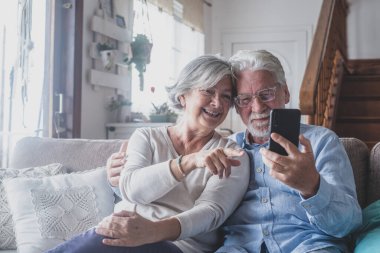 Samimi, olgun, yaşlı, evli bir çift arkadaşlarıyla seyyar görüntülü konuşma yapıyor. Yetişkin çocuklarla uzaktan iletişim kuruyor. Evde akıllı telefon uygulamaları kullanıyor..  