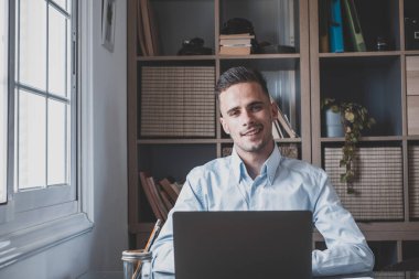 Video konferansında gülümseyen ve konuşan mutlu genç adam okulda ders çalışıyor ve öğreniyor. Millennial ev ödevi yapıyor. 