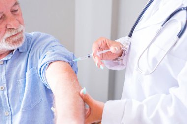 Kadın doktor, hastanedeki yaşlı erkek hastaya şırınga kullanıyor. Yaşlı bir adam klinikte grip aşısı oluyor. Tedavi merkezinde yaşlı ve hasta bir insanı aşılayan bir sağlık görevlisi.