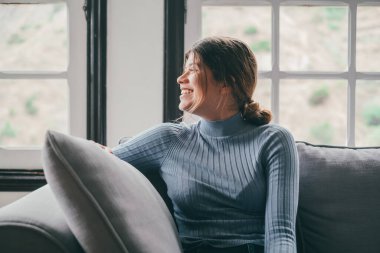 Evde gülüp eğlenen, pencereye bakıp gülümseyen ve eğlenen genç bir kadının portresi. 