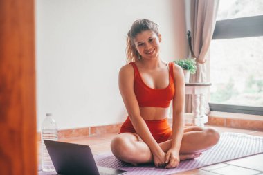 Sarışın güzel bir kadının portresi yoga yapıyor ve zihnini ve vücudunu evde yerde rahatlatıyor. Aktif ve sağlıklı bir kız sağlık eğitimiyle ilgileniyor. Güzel bir kadın kameraya bakıp gülümsüyor. 