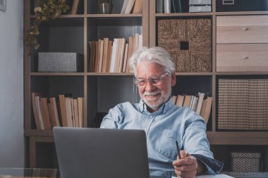 İnternette çalışırken gülümseyen Kafkasyalı mutlu iş adamı laptopta webinar podcast izliyor ve eğitim konferansını öğreniyor notlar alıyor çalışma masasına oturuyor, e-öğrenim kavramı oluşturuyor. 