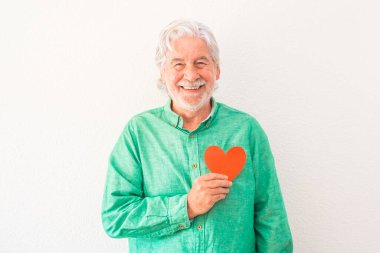 Göğsünde kırmızı bir kalple gülümseyen ve kameraya bakan olgun bir adamın portresi. Kalp sorunları ve hastalık konsepti olan bir adam.  