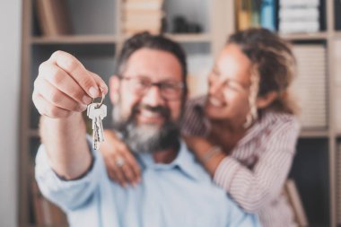 Heyecanlı genç eşlerin ev sahiplerinin tuttuğu anahtarlara odaklan. Mutlu evli çift yeni eve taşınmayı kutluyor, anahtarları gösteriyor, apartmanda duruyor, gayrimenkul ipoteği konsepti.... 