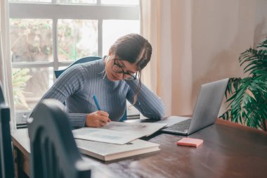 Evde ders çalışan ve ödevlerini yapan genç ve güzel bir kadın. İnternette bilgisayar ya da dizüstü bilgisayar kullanan genç bir kız..  