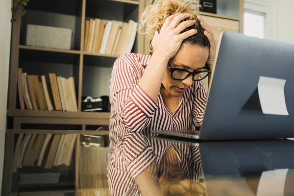 一个孤独 不快乐和悲伤的女人在办公室里用笔记本电脑 双手插在脑袋里看着它 压力大的女性有困难解决一个问题 — 图库照片