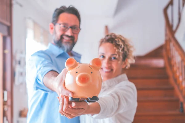 Portrait of happy caucasian couple holding piggy bank to save money to make their future dreams come true. Husband and wife holding piggy bank for savings at home while looking at camera