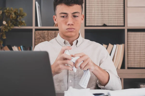 Unhappy young Caucasian teenager worker in glasses look at laptop screen shocked by gadget breakdown or operational problems. Frustrated man confused surprised by unexpected error on computer device.