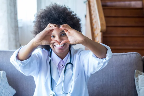 Woman physician doing heart shape gesture with hands. Smiling black female doctor making a love symbol using her hands. Healthcare worker expressing love and support to patients