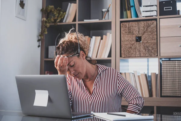 Exhausted female executive holding head in hand feeling lack of energy motivation while working on laptop at office. Upset depressed businesswoman in panic frustrated by bad news online on computer