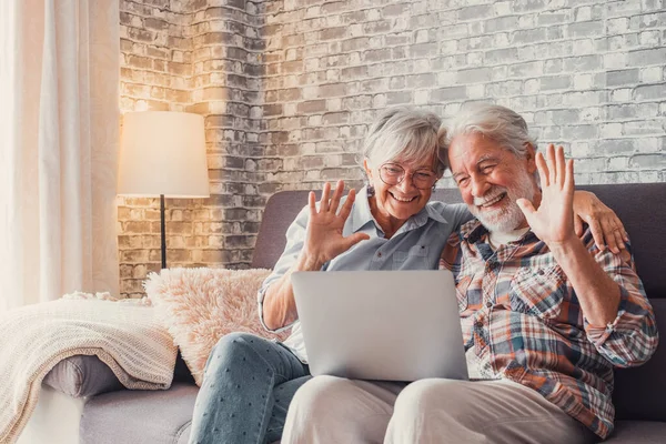 stock image Cute couple of old people sitting on the sofa using laptop together shopping and surfing the net. Two mature people in the living room enjoying technology talking in video call with friends or family. 