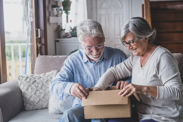 Happy mature aged older family couple unpacking carton box, satisfied with internet store purchase or unexpected gift, feeling excited of fast delivery shipping service, positive shopping experience.