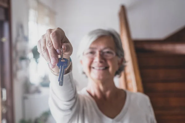 stock image Happy senior old aged woman customer landlord hold key to new house apartment give to camera, older retired female hand real estate owner make sale purchase property deal concept, close up view 