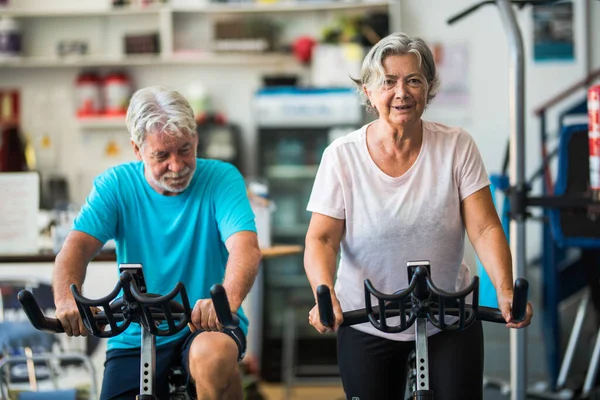 couple of mature people or active seniors doing exercise in the gym riding the bicycle indoor to be healthy - two happy retired with healthy lifestyle