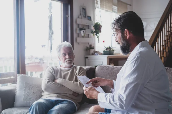 Erkek profesyonel doktor tıbbi bakım ziyareti sırasında kıdemli hastaya danışmanlık yapıyor. Genç bir doktor ve yaşlı bir ihtiyar kanepeye oturup tıbbi yardım sağlıyorlar. Yaşlılar evde bakım kavramı 