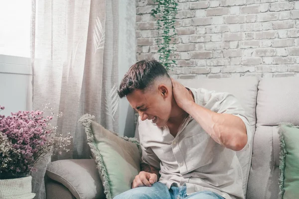 stock image Feeling pain in neck. Handsome young man massaging his neck while sitting on couch at home. 