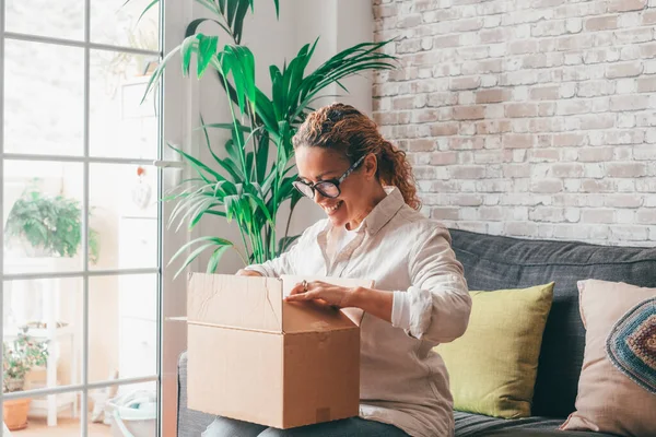 Overjoyed woman seated on sofa hold on lap small cardboard box open parcel client feels satisfied bought goods in internet, happy addressee received package from friend, quick delivery service concept