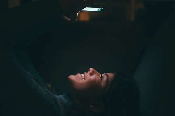 1人の美しい若い女性が笑顔で ソファの上で深夜に自宅で電話を使用しています 幸せな女性のティーンエイジャーは ネットサーフィンの友人とオンラインチャット テクノロジーとインターネットを楽しむ — ストック写真