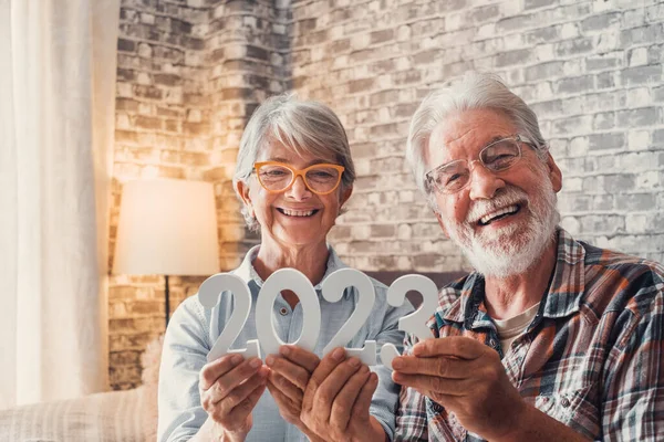 Portrait of couple of two old pensioners holding together numbers of 2023 at home. Close up of new year numbers, celebrating and goals for new life concept.