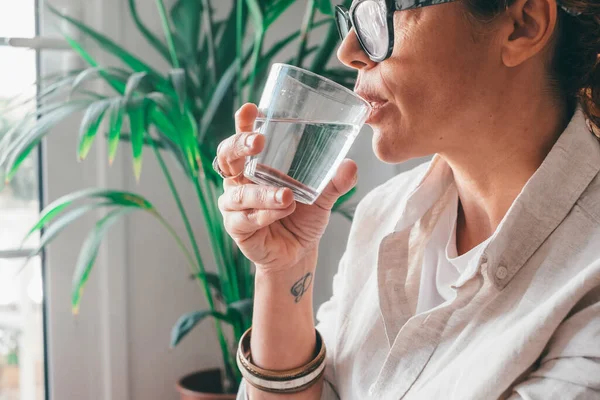 一个年轻女子在家里的房间里喝着一杯清水 加卡人口渴的女性拿着透明的玻璃杯在家里喝纯净水进行近距离采摘 — 图库照片