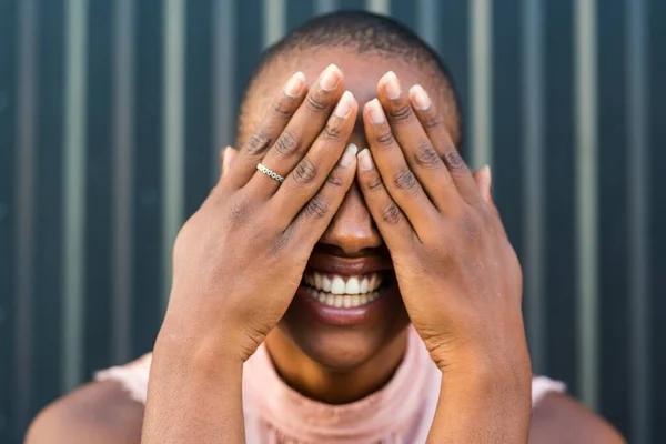 stock image portrait of one young and happy cheerful black african or american woman smiling at the camera with her hands on her eyes covering it 