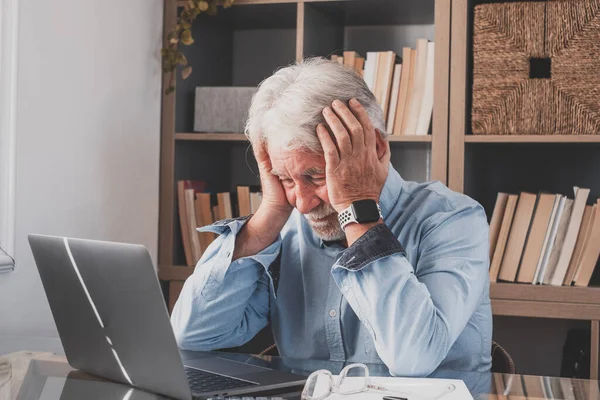 stock image Unhappy frustrated old businessman holding head in hands feeling depressed of having financial trouble. Senior man working at home office using laptop, desperately stressed because of workload