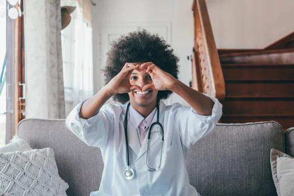 Woman physician doing heart shape gesture with hands. Smiling black female doctor making a love symbol using her hands. Healthcare worker expressing love and support to patients