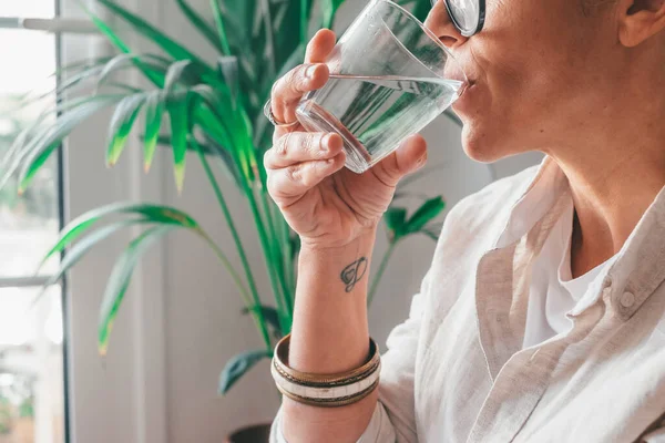 一个年轻女子在家里的房间里喝着一杯清水 加卡人口渴的女性拿着透明的玻璃杯在家里喝纯净水进行近距离采摘 — 图库照片