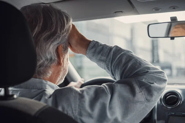 Stressed old businessman feeling headache in car, stop the car, keeping hand to head and feeling anxiety.