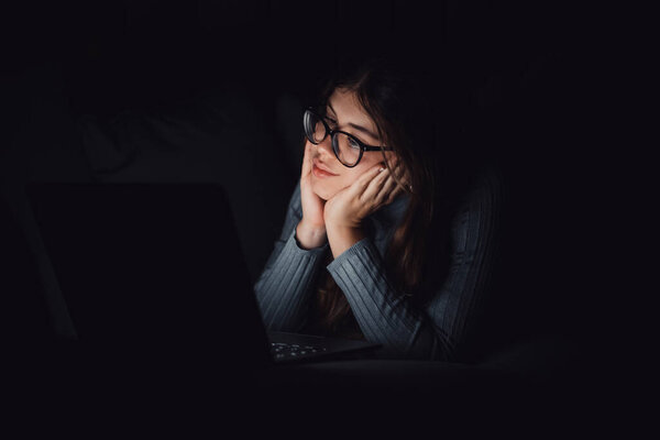 Одна счастливая жизнерадостная молодая женщина, пользующаяся ноутбуком поздно вечером в гостиной на диване дома. Онлайн-девушка в сети, пересматривает социальные сети. Улыбающийся подросток, использующий технологии и интернет. 