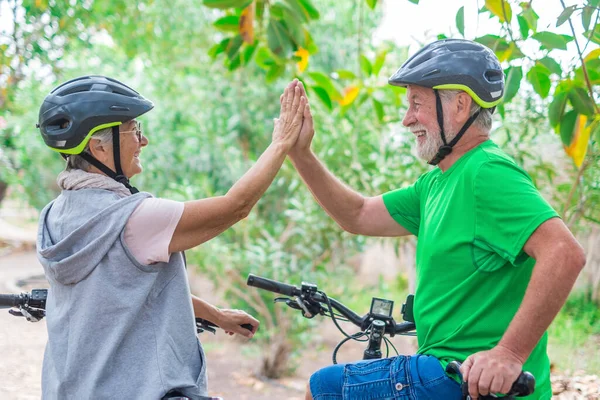Couple of two seniors giving five together outdoors having fun with bicycles enjoying nature. Couple of old people building a healthy and fit lifestyle.