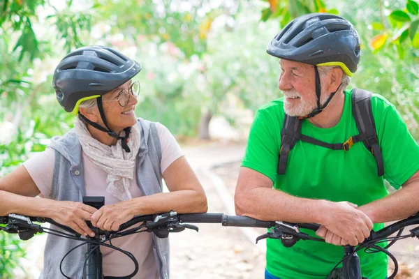 Portrait of couple of old and happy in love seniors looking each other smiling and having fun with their bikes in the nature outdoors together feeling good and healthy.