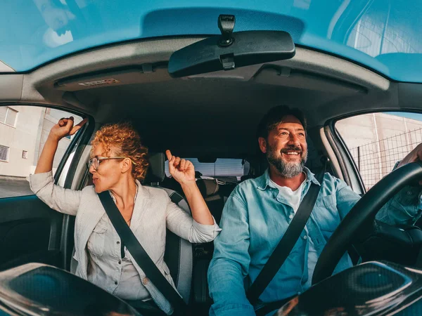 Couple of happy people dancing and singing in the car driving and traveling with a vehicle in the street enjoying their lifestyle having fun.