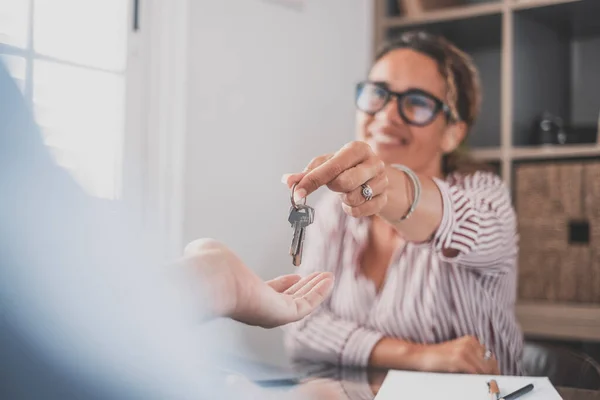 stock image Smiling female realtor agent giving keys to apartment buyer. Homeowner receiving their new house key from a real estate agent at office. Happy saleswoman giving house keys to customer 